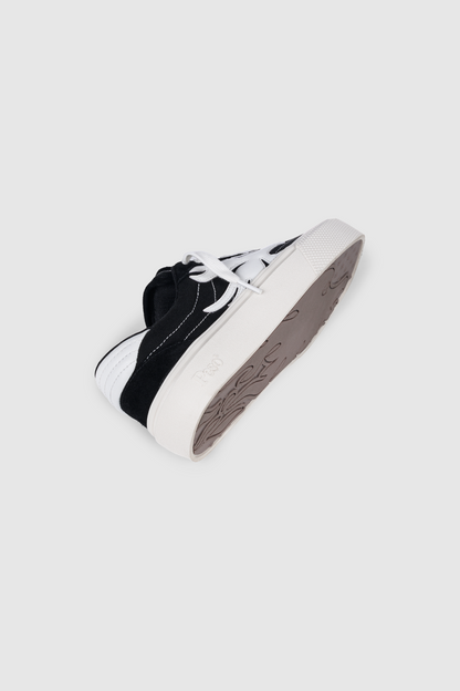 The PESOCLO Peso Skate sneaker is presented at an angle against a plain light background, highlighting its black and white colorway, white laces, thick textured sole, and distinctive side stripe design. Crafted from a premium canvas-suede mix for enhanced comfort and style, this shoe also features unique artwork accents on the upper for added individuality.