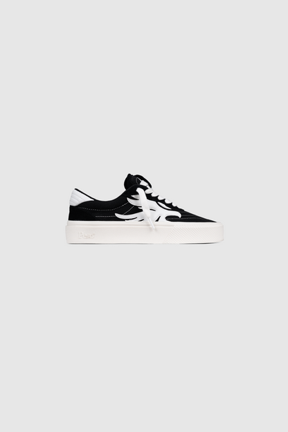 The PESOCLO Peso Skate is a black and white low-top sneaker crafted from a canvas-suede mix, featuring white laces, a white sole, and a bold white design on the side. It is displayed on a plain light gray background.