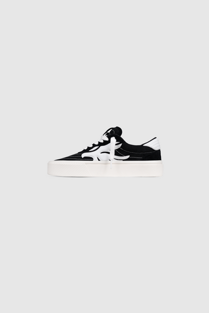 The Peso Skate by PESOCLO is a black and white low-top sneaker featuring a canvas-suede mix artwork upper, white laces, a signature white side stripe, and a thick white sole, shown against a plain gray background.