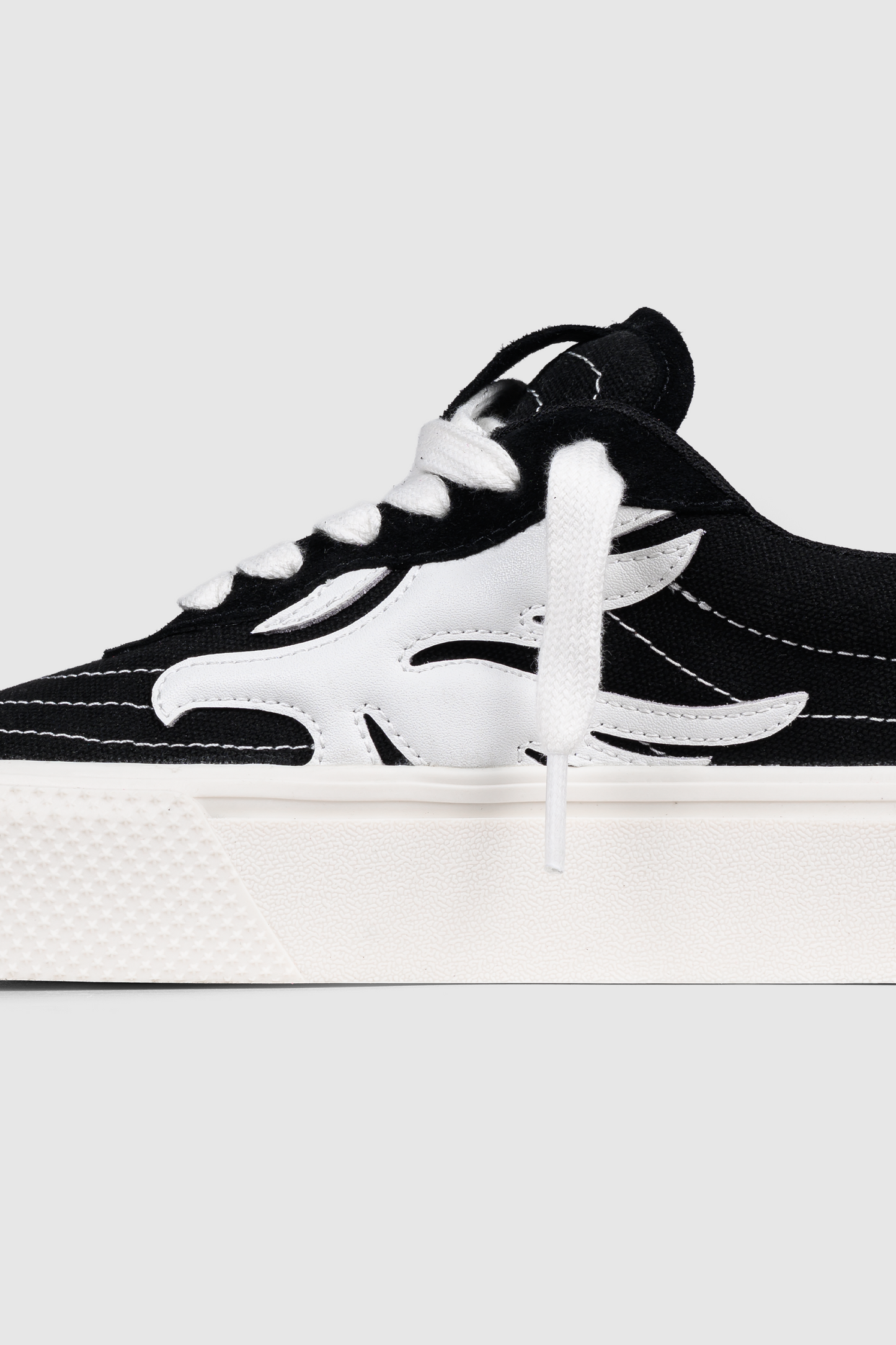 A close-up of the PESOCLO Peso Skate sneaker showcases a bold artwork upper, white laces, contrasting white stitching, and a thick white sole. The shoe is highlighted by a distinctive white flame-shaped design on the side.