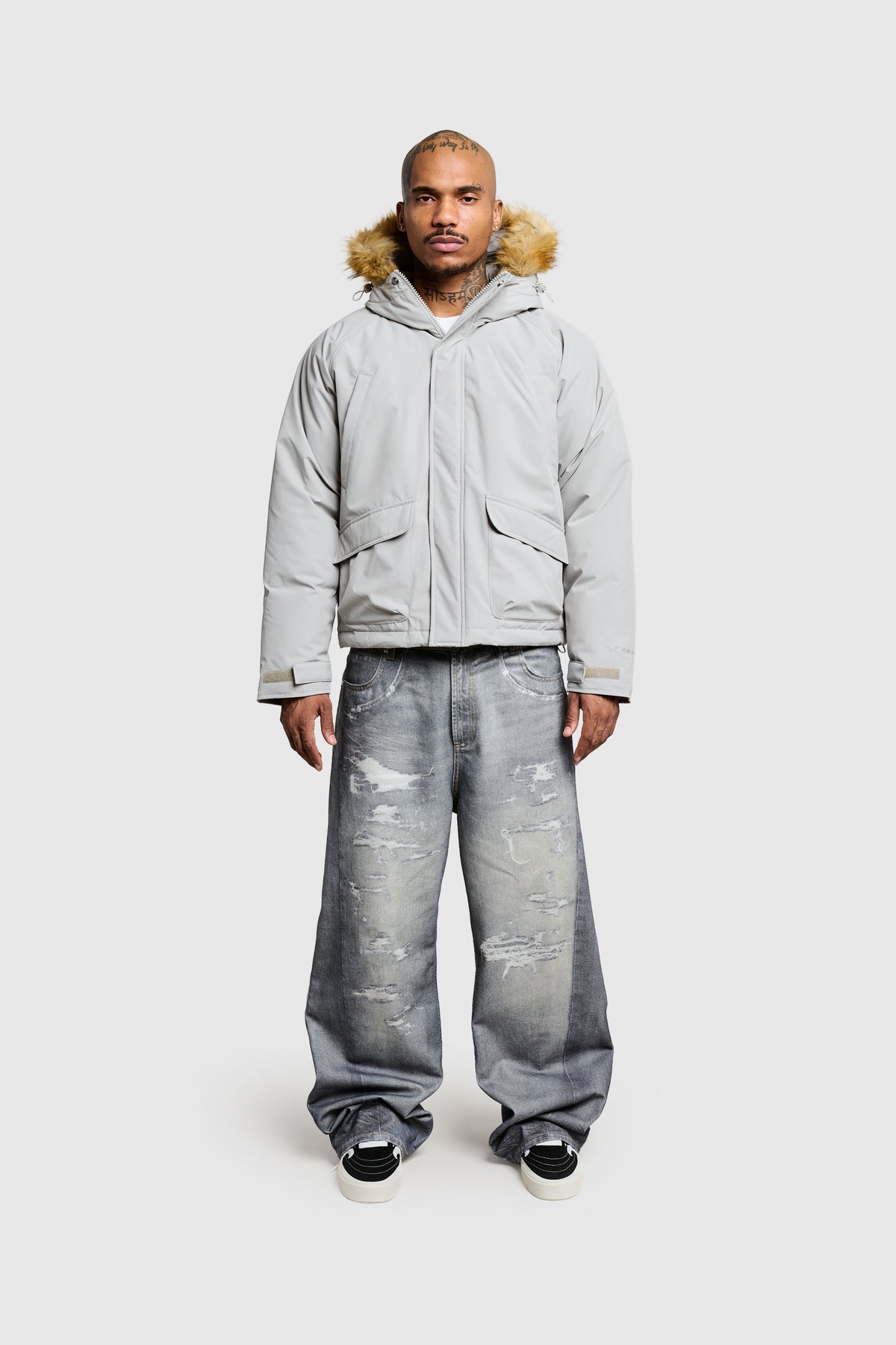 A person wearing the PESOCLO Fur Parka—a light gray hooded winter jacket with a faux fur collar—along with baggy, distressed jeans and black-and-white sneakers stands against a plain white background.